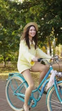 Işıl ışıl gülüşü olan ışıl ışıl bir kadın güneşli bir günde parkta bisiklet sürmekten zevk alıyor. Hasır şapka ve günlük yaz kıyafetleri giyiyor.