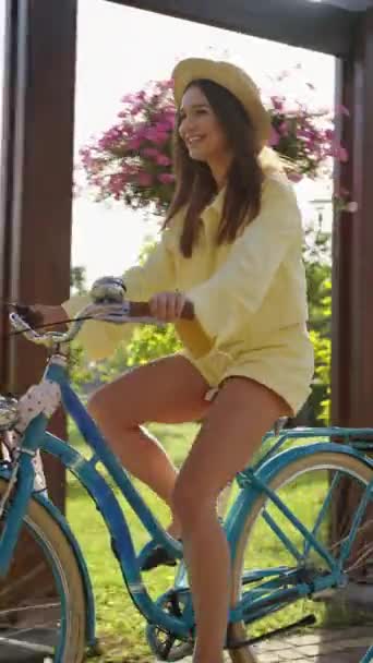 戴着草帽 穿着黄色衬衫 骑着蓝色老式自行车 背景是粉色花朵和绿色的微笑女人 温暖的阳光增强了悠闲自在乘坐的愉快 无忧无虑的氛围 — 图库视频影像