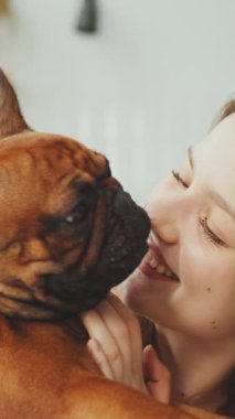 Neşeli kadın, Fransız Bulldog 'u parlak mutfakta yüzünü yalarken yürekten gülüyor. Sevgi ve mutluluk dolu evcil hayvan ve sahibi arasında özel bir bağ vardır.