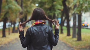 Genç bir kadın sonbahar günü ağaçlarla kaplı şehir caddesinde yürüyor, neşeli bir şekilde saçlarını çeviriyor.