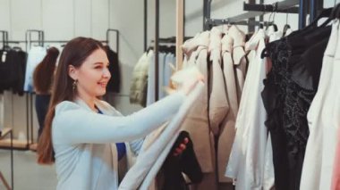 Şık spor ceketli genç bir kadın moda mağazasındaki çeşitli kıyafetlere hevesle göz atıyor. Alışverişin ruhu.