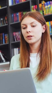 Genç bir kadın, video görüşmesi sırasında, kitaplıkların arkaplanına karşı etkin ve açıklayıcı ifadeler kullanıyordu. Etkileşimli çevrimiçi öğrenme kavramı