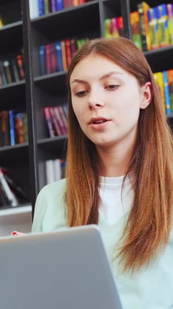在视频通话中 年轻女性在书架的背景下清晰地表达自己的观点 积极地表达自己的观点 交互式在线学习概念 — 图库视频影像