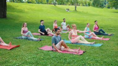 Canlı yeşil parktaki renkli paspaslar üzerinde yoga oturumunu gevşeten çeşitli bireyler topluluğu, ortak egzersiz deneyiminin tadını çıkarıyorlar.