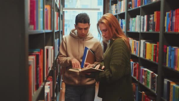 Двоє Студентів Поглинули Книгу Бібліотеці Поділившись Знаннями Обговореннями Між Полицями — стокове відео