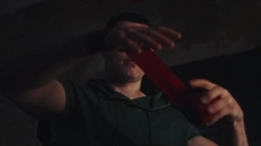 Erkek boksör karanlık odada ellerini kırmızı spor bandajlarıyla sarıp antrenmandan önce konsantre oluyor.