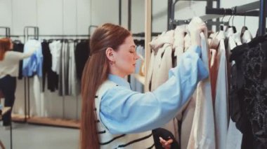 Genç alışveriş düşkünü kadın moda mağazasından çeşitli kıyafet parçaları seçiyor. Koleksiyonuna ekleme yapmadan duramıyor.