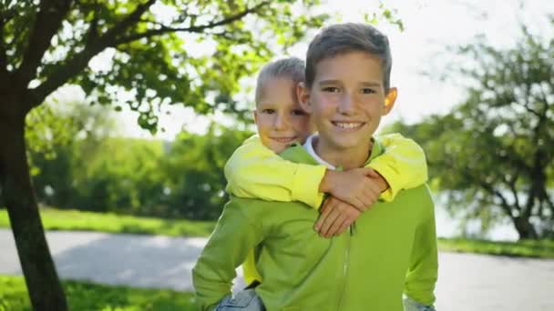Older Boy Carries His Younger Brother Piggyback Style Both Smiling — Stock Video