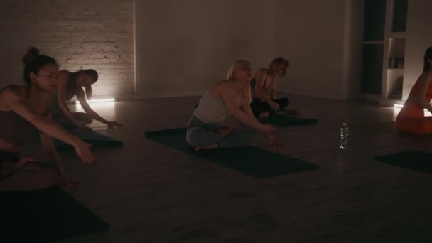 一组妇女参加瑜伽课 在灯光温暖 砖墙围成的工作室里 在垫子上表演侧身伸展动作 促进柔韧和放松 — 图库视频影像