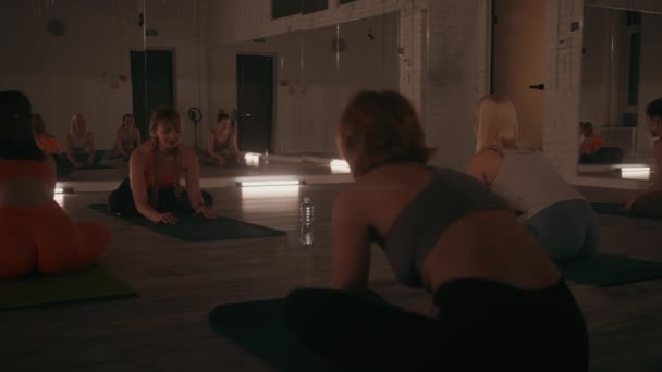 妇女在夜间瑜伽课上在灯光柔和的演播室里进行伸展运动 反映出集中注意力和宁静的锻炼环境 — 图库视频影像