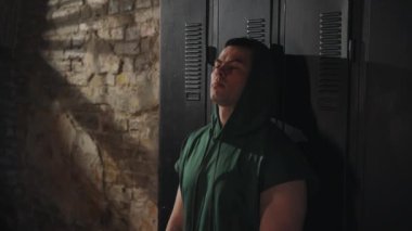 Yorgun boksör, loş ışıklı spor salonundaki dolabın karşısında ellerini yüzüne sürerek ringe çıkmadan önce derin bir yansıma ve zihinsel hazırlık yapıyor.