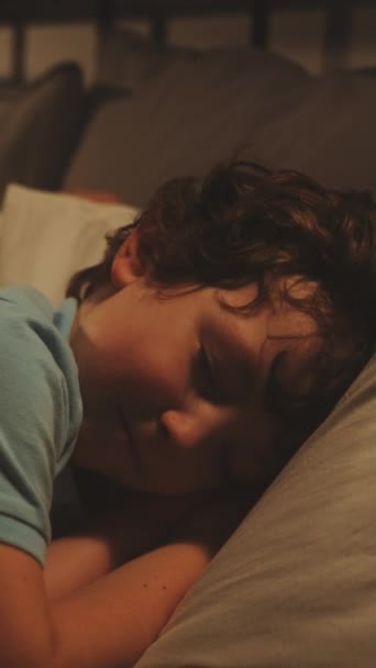 縦スクリーン 青いパジャマを身に着けている若い男の子は 彼のテディベアが彼の横に横たわっているので 眠りを見つけるのに苦労しています — ストック動画