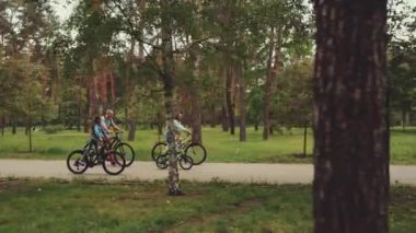 Aile, orman parkında birlikte dolaşır. Açık hava aktivitelerinin tadını çıkarırlar. Ebeveynler ve çocuklar ağaçlar ve yeşilliklerle çevrili asfalt yol boyunca bisiklet sürüyorlar, sağlıklı ve aktif yaşam tarzını teşvik ediyorlar.