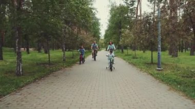 İki çocuklu bir aile, parkta ağaçlık patika boyunca bisiklet sürmekten ve aktif bir aile hayatı sürmekten keyif alıyor. Neşeli bir birliktelik ve aktivite anı