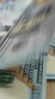 100 dolarlık banknotlar bir tomar para içinde dönen masanın üzerine düşüyor. Ek banknotlar yağdıkça daha da büyüyen bir yığın para. İş ve finans kavramı