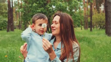 Anne ve oğlu yemyeşil bir parkta birlikte karahindiba üfleyerek dışarıda eğleniyorlar. Doğa ve aile bağı kavramı