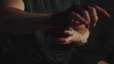 Boks antrenmanından önce ellerini kırmızı bandajlarla saran bir adam. Erkek, yoğun antrenman ya da maç için hazırlanıyor, bilek korumasına odaklanıyor. Güç ve uygunluk kavramı.