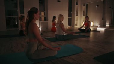 Yoga ve meditasyon yapan bir grup kadın loş bir stüdyoda rahatlama ve farkındalığa odaklanıyor. Sakin atmosfer ve rahat pozlar. Farkındalık, rahatlama ve zindelik kavramı