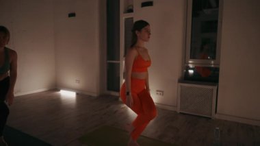 Yoga eğitmeni, loş ışıkta yoga minderlerinde kartal pozu veren sınıftan bir kadın. Ilık aydınlatma ve aynalar sakin atmosferi güçlendirir. Denge ve konsantrasyon kavramı