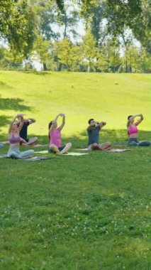 Dikey Ekran: Parkta grup yoga oturumu, katılımcıların minderlere oturması, eğitmenin rehberliği altında ileriye doğru esnemeleri. Toplumsal refah ve farkındalık kavramı