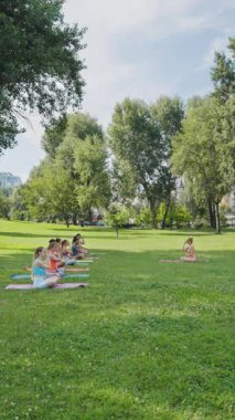 Dikey Ekran: Eğitmen dışarıdaki bir grup insan için nefes alma uygulamalarını yönetiyor. İnsanlar parkta paspaslara oturur. Sağlık, meditasyon ve rahatlama kavramı