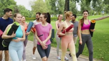 Yoga minderleri taşıyan bir grup insan parkta yoga dersinden ayrılıyor. Zindelik, toplum ve refah kavramı.