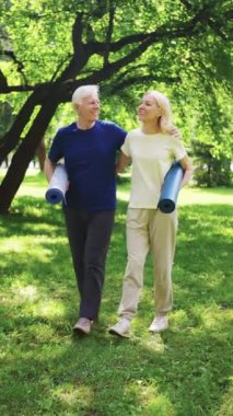 Yaşlı çift parkta birlikte yürüyor, yoga minderleri taşıyorlar, temiz havanın ve birbirlerine eşlik ediyorlar. Aktif yaşam tarzı, sağlıklı yaşlanma ve altın yıllardaki arkadaşlık kavramı