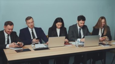 İş adamları iş molasında konferans masasında oturuyorlar, hepsi akıllı telefonlarına odaklanmış. Mobil bağımlılık ve iş yerindeki dikkat dağınıklığının etkisi. Taşınabilir bağımlılığı kavra