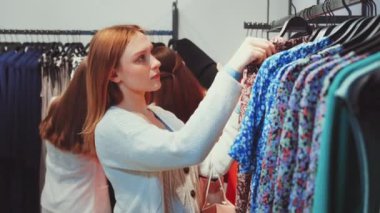 Bir mağazada farklı kıyafet seçeneklerini inceleyen bir kadın mükemmel bir kıyafet bulmaya odaklanmış. Alışveriş, moda, perakende deneyimi ve yeni kıyafetler seçme zevki