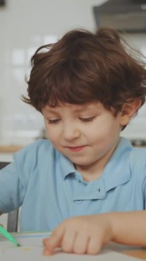Dikey ekran: Genç çocuk masadaki boya kalemleri ve kalemlerle çizim yapmaya odaklandı. Yaratıcı aktiviteler ve erken eğitim kavramı. Evde öğrenme ve yaratıcılık
