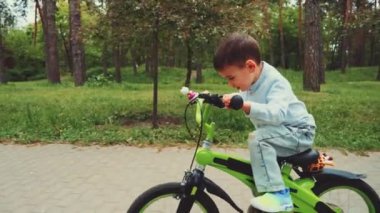 Küçük çocuk parkta yeşil bisiklete biniyor, gidona odaklanmış. Kot giymiş, dışarıda eğleniyor. Çocukluk keşfi, eğlence ve bisiklet öğrenme kavramı