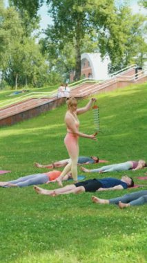 Dikey Ekran: Yoga eğitmeni, katılımcıları meditasyon sırasında derin bir rahatlamaya yönlendirmek için rüzgar çanları kullanıyor. Parktaki paspasların üzerinde yatan katılımcılar. Sağlıklı iyileşme ve farkındalık kavramı