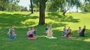 Yoga sınıfı, sakin bir park ortamında tekne pozu çalışıyor. Katılımcılar paspaslar üzerinde dengelenmiş, çekirdek kaslarını çalıştırıyorlar. Açık hava grup fitness ve refah kavramı