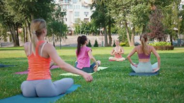 Yoga grubu parktaki paspaslar üzerinde oturarak omur bükme egzersizi yapıyor. Katılımcılar esnekliği artırmak için gövdelerini büküyorlar. Açık hava yoga ve sağlıklı yaşam tarzı kavramı