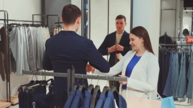 Mağazada mavi ceketi deneyen bir adam. Kadının uyum sağlamasına yardım ediyor. Ayrıntılı görüş gösteren aynalı yansıma. Alışveriş, moda ve uygun yardım kavramı