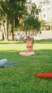 Dikey Ekran: Yoga meraklıları şehir parkındaki paspaslar üzerinde esneme egzersizleri yapıyorlar, fiziksel aktivite ve sakin açık hava ortamının kombinasyonu. Sağlık ve Sıhhat kavramı