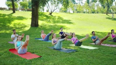Park 'taki yoga seansına katılan grup tekne duruşu yapıyor, çekirdek dayanıklılığını ve dengesini arttırıyor. Açık hava fitness ve toplum refahı kavramı