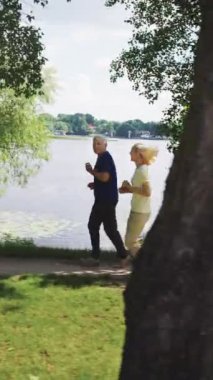Güneşli bir günde sakin göl kenarında koşan yaşlı çift. Kıdemli fitness anlayışı, sağlıklı yaşam tarzı ve doğanın keyfi.