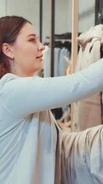 Kadın mağazada birkaç parça kıyafet tutuyor, daha fazla seçeneği incelerken gülümsüyor. Alışveriş bağımlılığı, moda tutkusu, perakende terapisi ve yeni kıyafetler seçmenin keyfi.