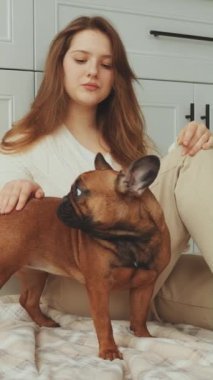 Mutfak zemininde köpeğiyle oturan bir kadın, nazikçe Fransız Bulldog 'unu okşuyor. Günlük hayatta evcil hayvan bakımı, rahatlık ve arkadaşlık kavramı. Sahibi ve evcil hayvanı arasındaki bağı vurgula