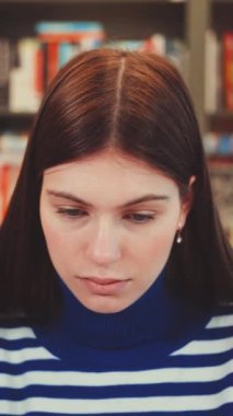 Dikey ekran: Çizgili kazaklı öğrenci kütüphanedeki işine odaklanıyor. Konsantrasyon ve akademik adanmışlık kavramı