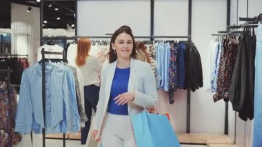 Kadın, arka planda arkadaşları olan bir giyim mağazasında alışveriş yaparken mutlu bir şekilde alışveriş yapıyor. Eğlence alışverişi, moda, perakende terapi ve arkadaşlık kavramı