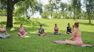 Pranayama teknikleri uygulayan bir grup. Açık hava yoga seansı sırasında, yemyeşil park ortamında. Katılımcılar paspaslara oturup kontrollü nefes alma ve iç huzura odaklanıyorlar. Toplumun refahı kavramı