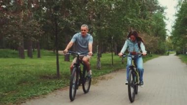 Çift parkta bisiklete binmeyi seviyor. Ağaç çizgili yolda yürürken gülümsüyor ve konuşuyor. Açık hava aktiviteleri, bağlılık ve sağlıklı yaşam tarzı kavramı