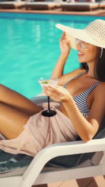 Kadın bilardo oynuyor, güneş şapkası ve çizgili bikini giyerken ferahlatıcı bir kokteyl yudumluyor. Yaz tatili, boş zaman ve eğlence. Tatil kavramı, lüks ve tasasız anlar.