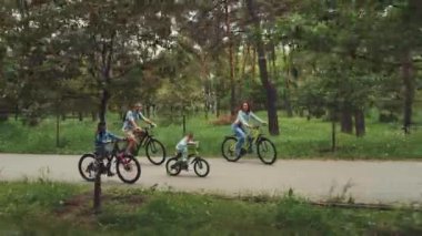 Yeşillik ve ağaçlarla çevrili park yolunda birlikte bisiklete binen dört kişilik aile. Aile bağları kavramı açık hava macerası ve sağlıklı yaşam tarzı
