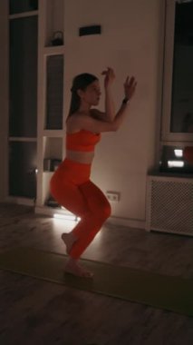 Dikey ekran: Yoga eğitmeni, yoga minderleri üzerinde kartal pozu veren birinci sınıf bir kadın. Ilık aydınlatma ve aynalar sakin atmosferi güçlendirir. Denge ve konsantrasyon kavramı