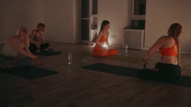 Yoga dersi sırasında loş bir stüdyoda esneyen kadınlar esneklik ve farkındalığa odaklanıyorlar. Rahatlama, sağIık ve farkındalık kavramı