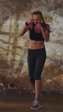 Sporcu formalı bir kadın, şehir stili spor salonunda duvar arkası tuğlalı boks talimi yapıyor. Güçlü fizikte kararlılık, zindelik ve güç vurgulanır