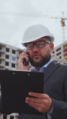Dikey Ekran: Sakallı adam, kasketli ve takım elbiseli, telefonda çok katlı binalara karşı konuşuyor. İnşaat alanında inşaat mühendisi. İletişim kavramı